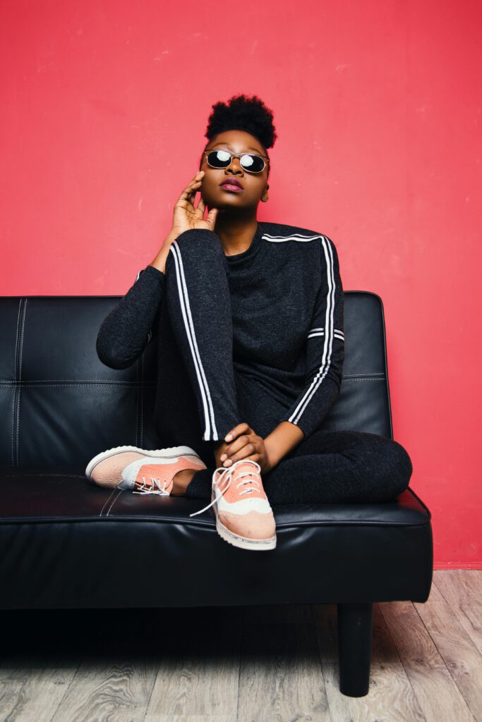 Fashionable woman posing confidently on a sofa in a modern studio setting.